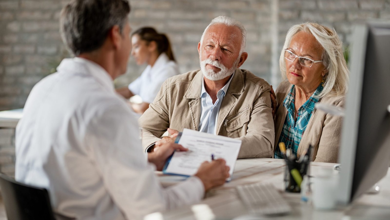 Senior couple consulting with healthcare worker about their insurance policy while having a meeting at clinic.